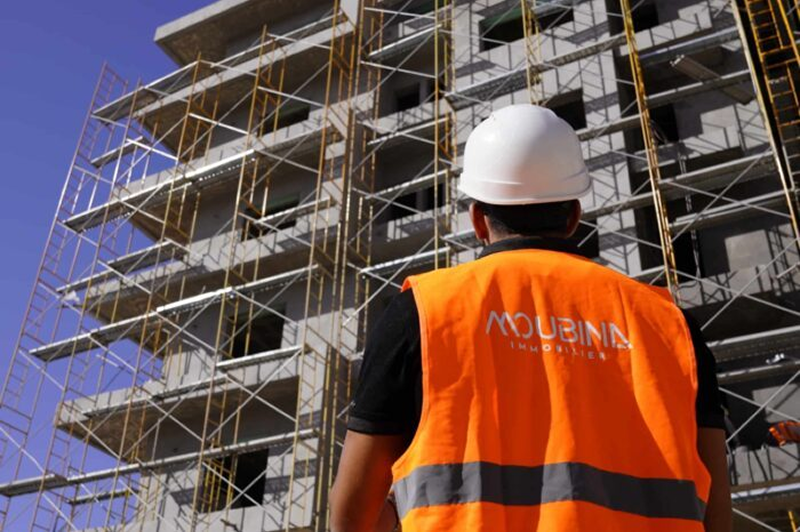 Chantier de construction avec échafaudages et ouvrier en tenue de sécurité orange